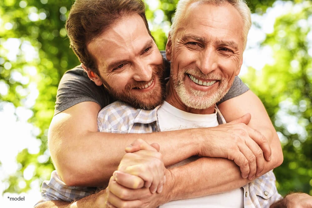Middle-aged man and his mature father, smiling and hugging outside.