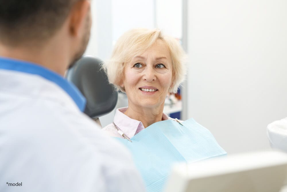 Older woman in dentist chair, talking to the dentist.
