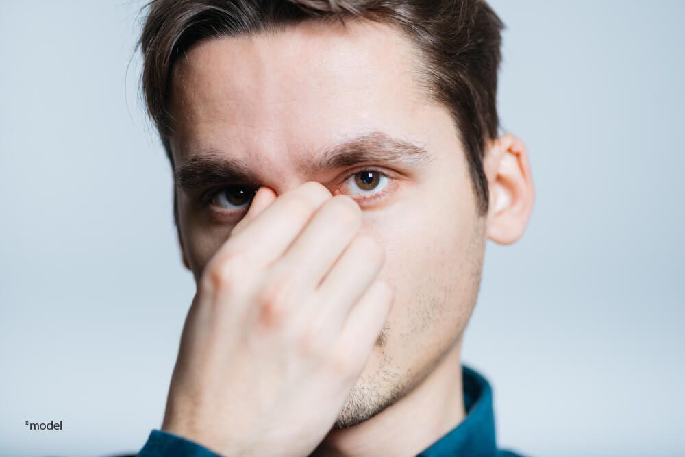 Young man holding bridge of his nose, looking into the camera.