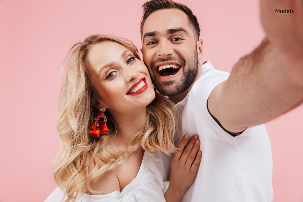 attractive cheerful young couple in love standing together isolated over pink background, taking a selfie-img-blog