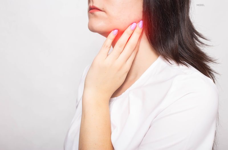 Woman with hand on a neck, which is glowing red to demonstrate jaw and neck pain.