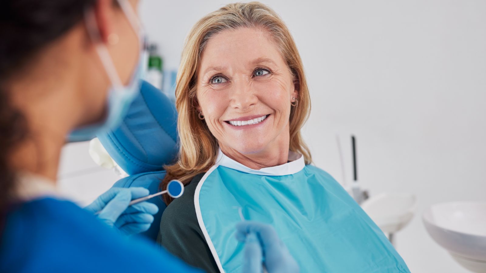 Woman sitting in a dental office smiling at an assistant