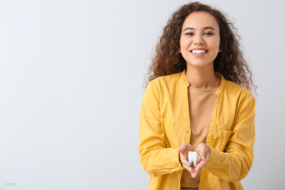 A smiling woman in yellow holding a model of a tooth